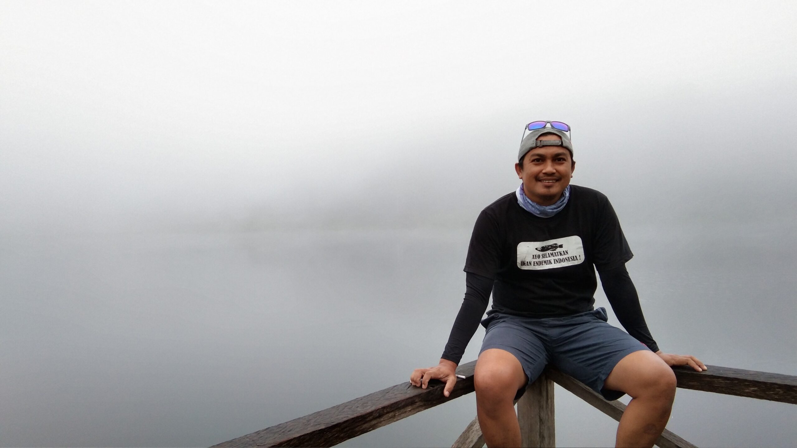 A photograph of Abdul Gani in athletic clothes sitting on a fence in front of a misty view.
