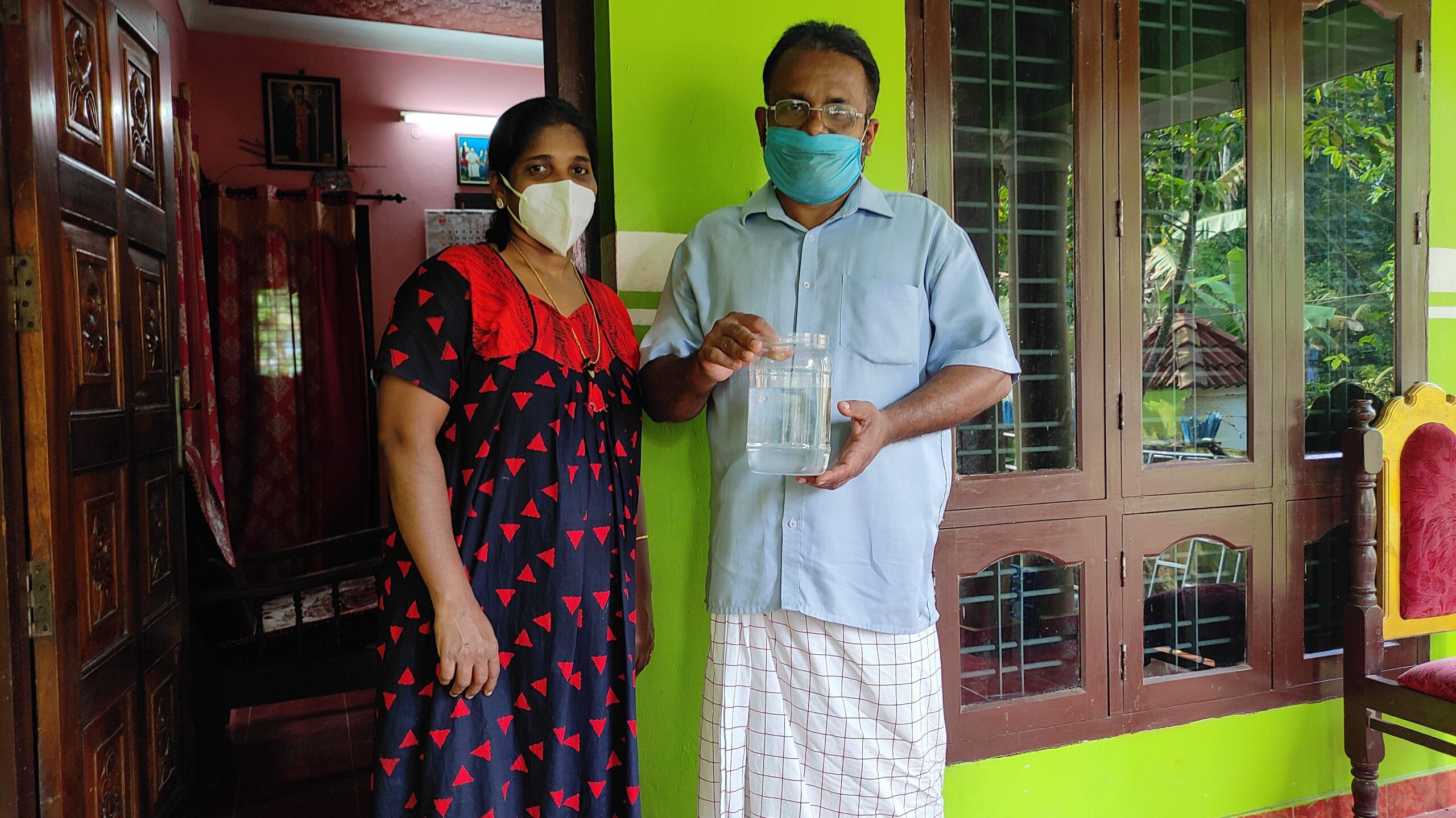 A photograph of a man and a woman standing outside a building holding a jar of water with a fish in it.